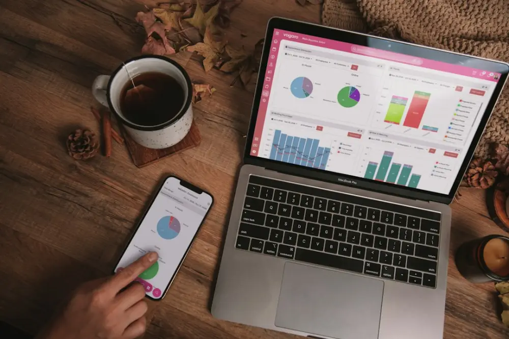 A laptop and smartphone displaying analytics dashboards on a wooden desk with a mug, illustrating performance evidence